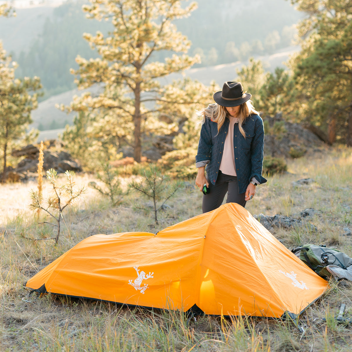 Orange Bivy Tent with Rain Fly and woman standing next to the tent in the mountains